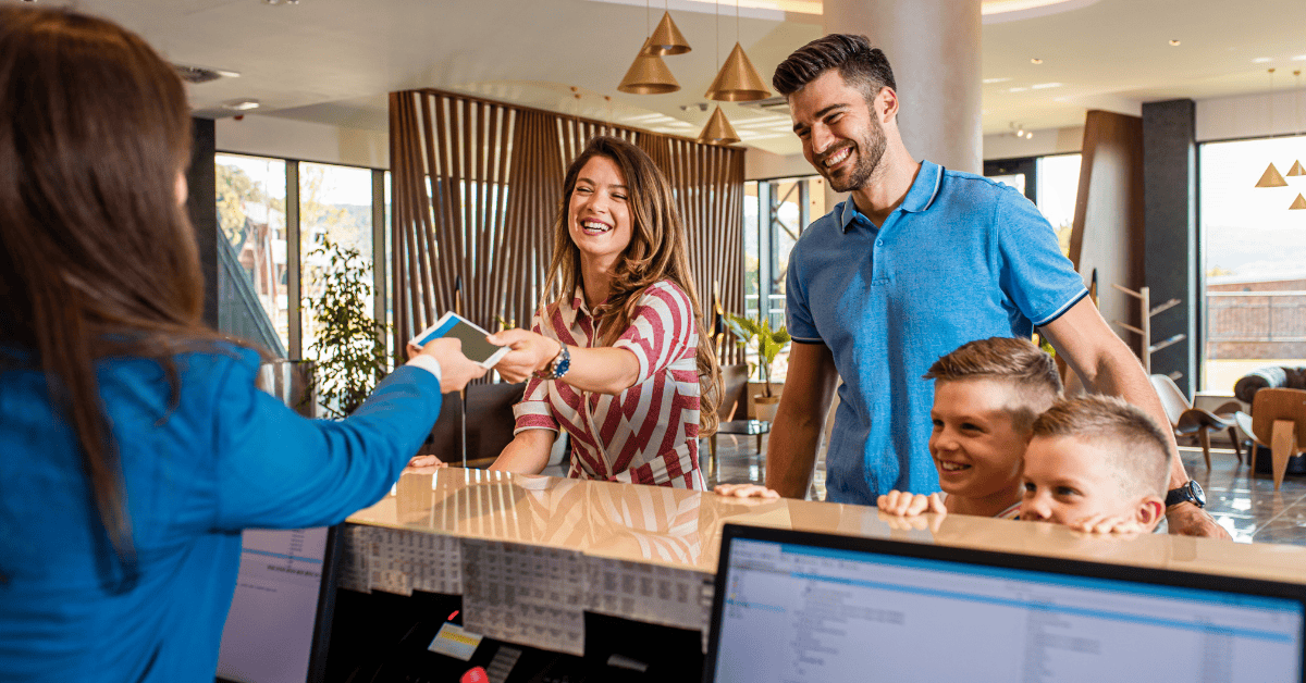 Happy couple with two young boys checking into a hotel.