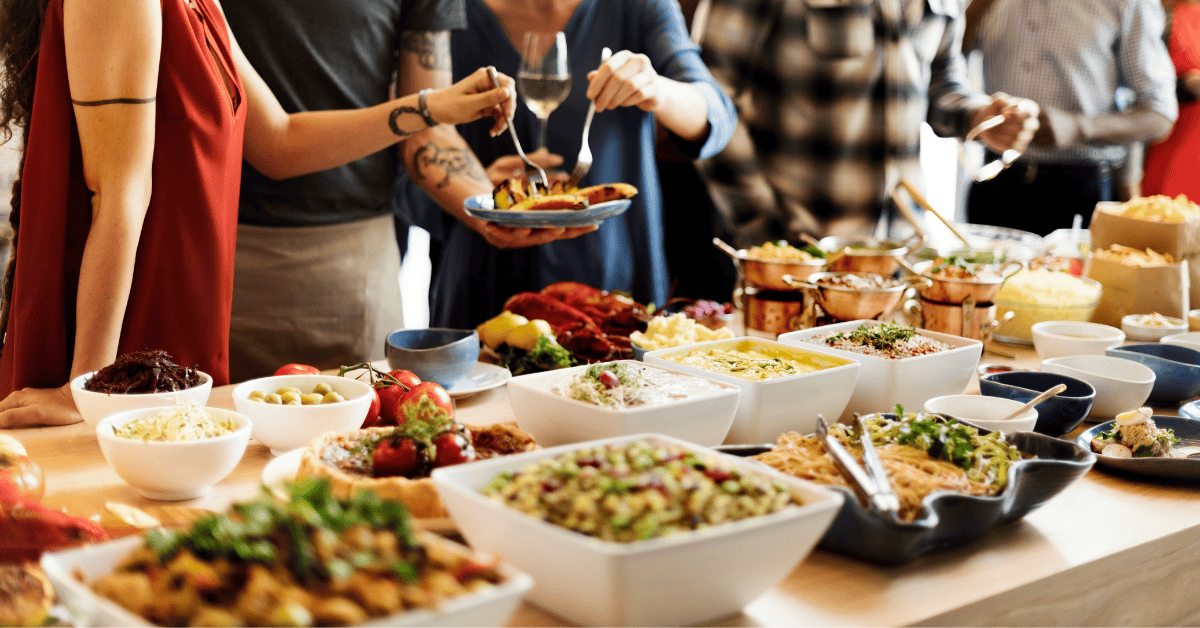 Groups of people serving themselves a plate of food from a buffet of colorful food on a table.