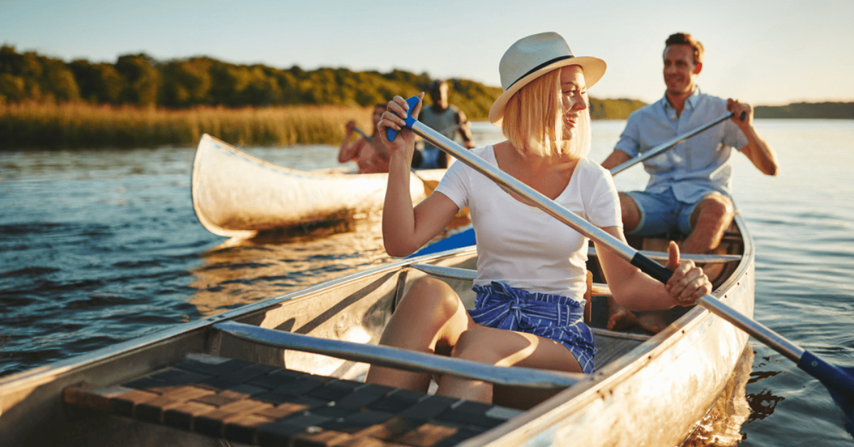 Couple rowing a canoe on a lake with trees at sundown.