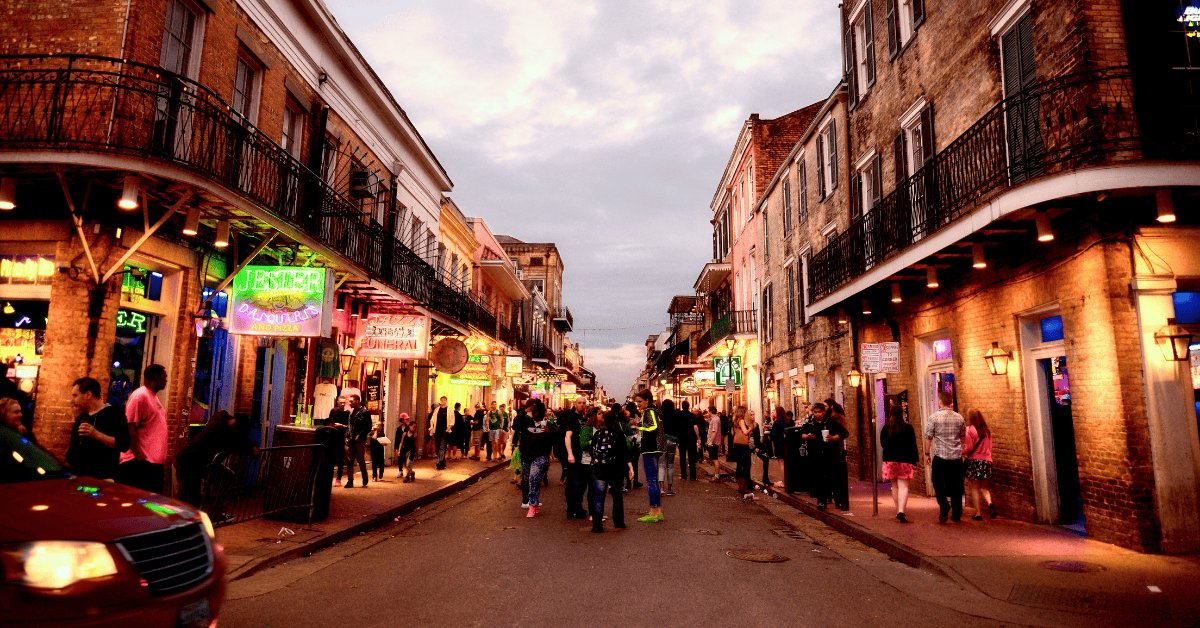 GroupSync | New Orleans for Group Travel | Busy street in the French Quarter lit up with bar and restaurant signs and people walking in the street