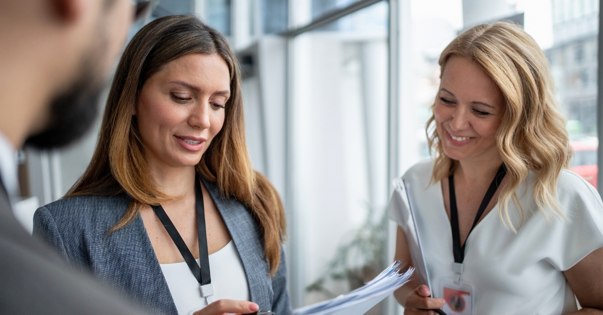 Businesswomen wearing lanyard showing clipboard to businessman at conference