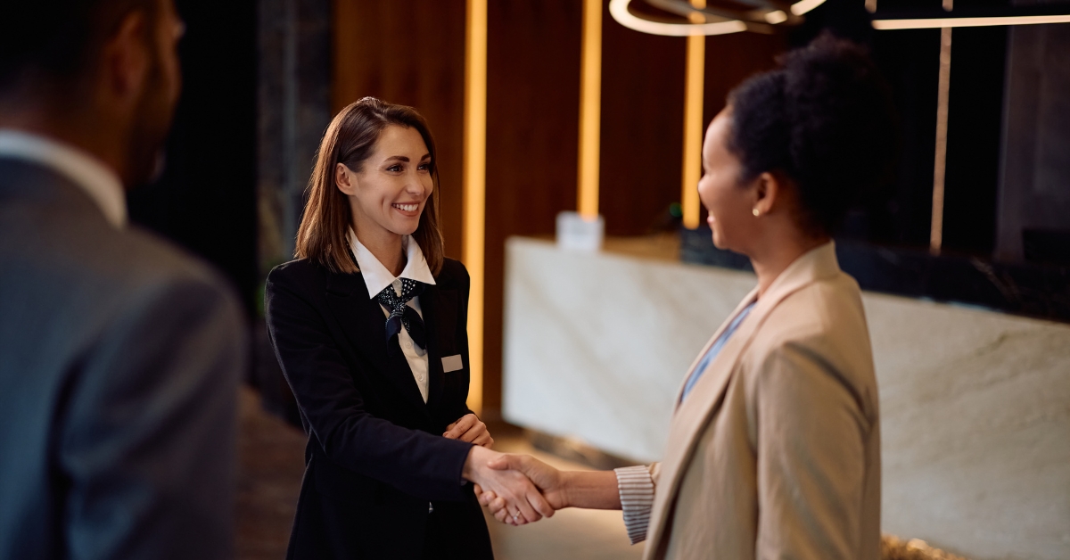 Happy female concierge greeting a businesswoman planner handshake in hotel lobby