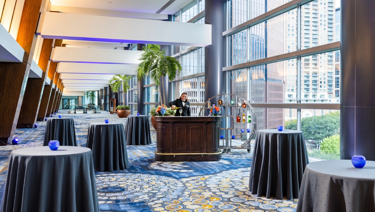 Hilton Americas-Houston woman at bar in meeting hall with round table setup